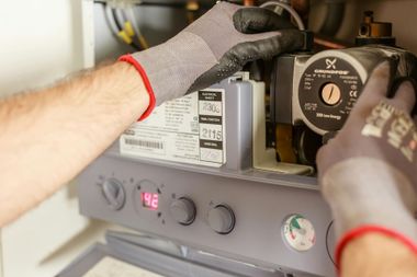 Gloved hands adjusting a boiler control panel with a digital display and circular gauge.