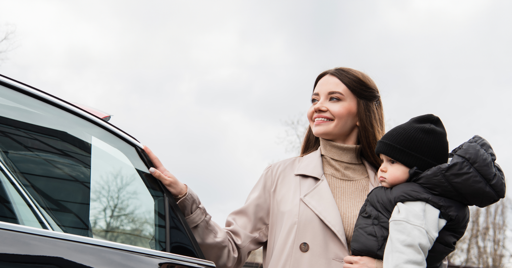 Woman holding a small child outdoors next to a car