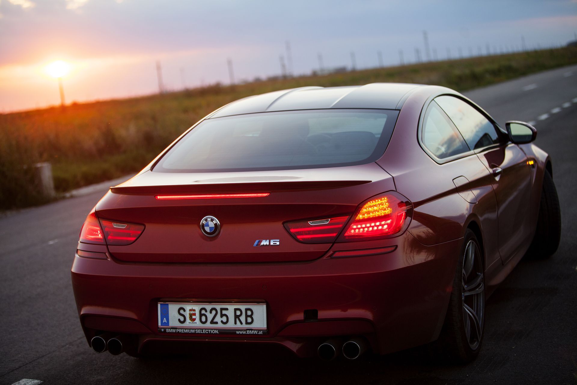 A red bmw is parked on the side of the road at sunset.