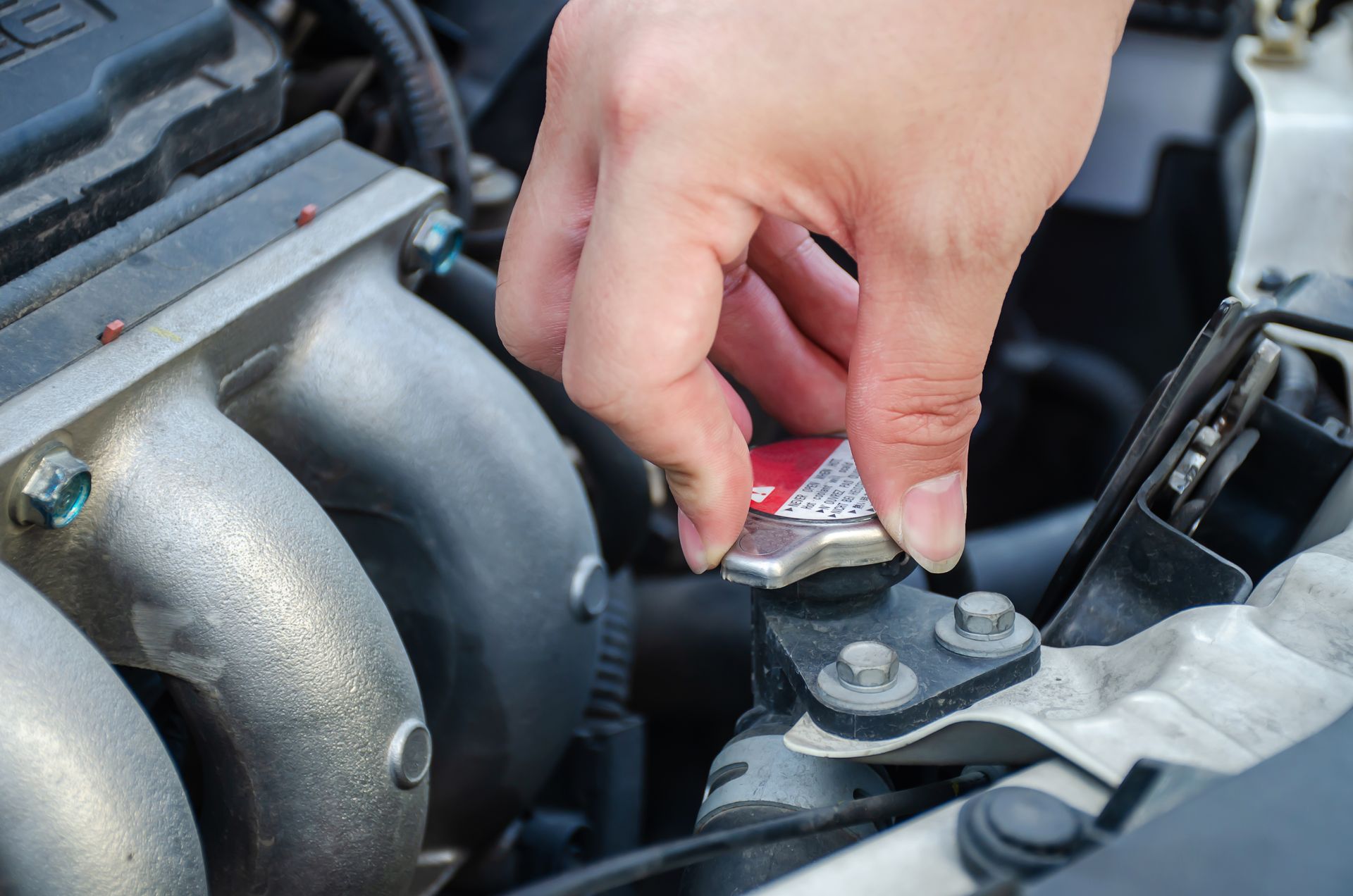 A person is opening a radiator cap on a car engine.