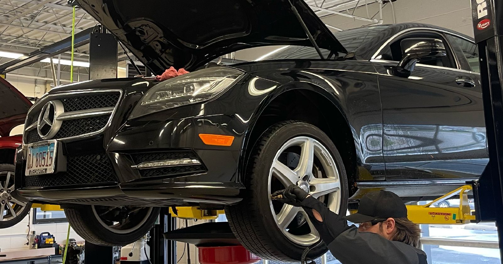 A man is working on a black mercedes benz on a lift in a garage.