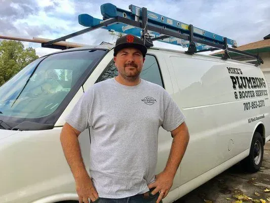 A man is standing in front of a white van with a ladder on top of it.