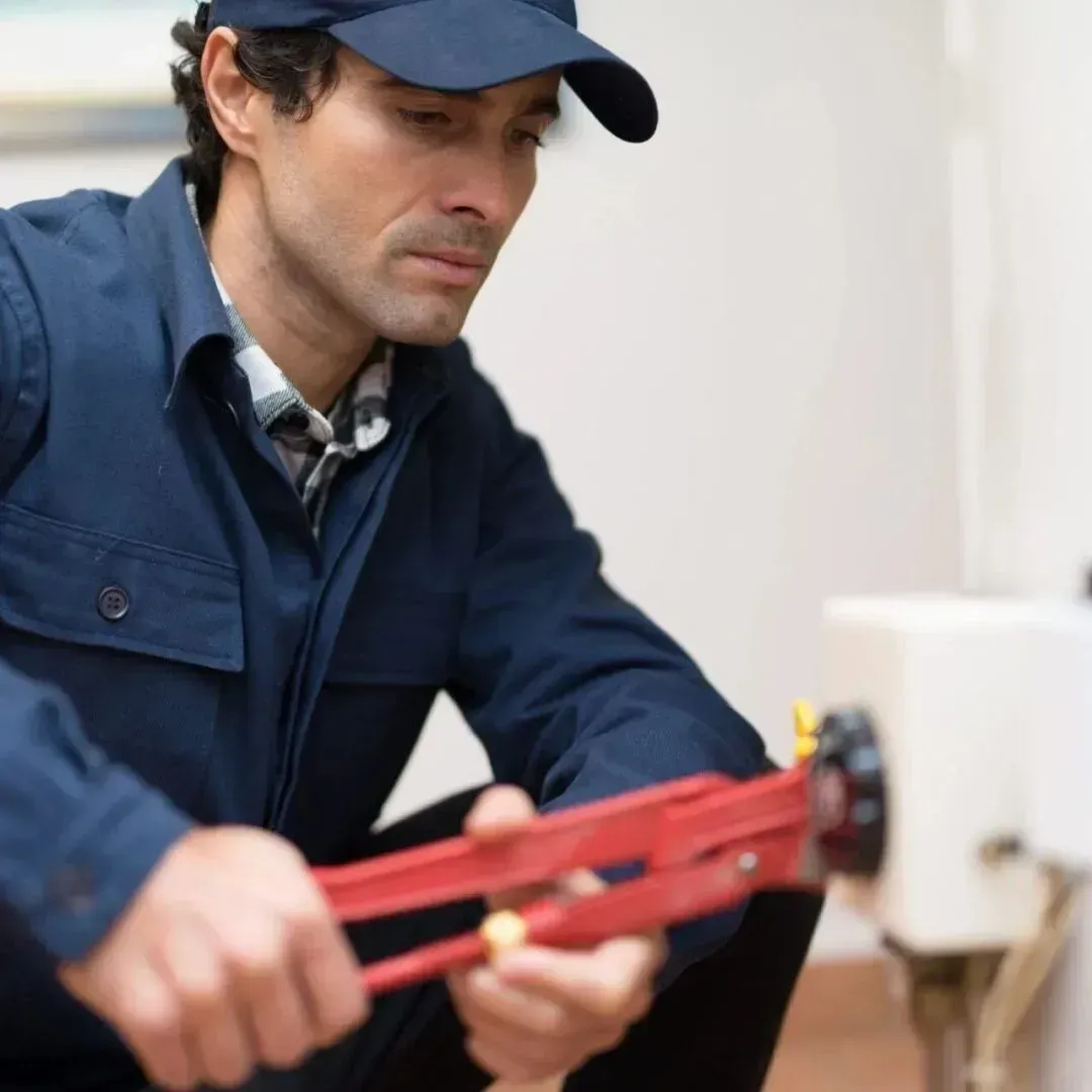 A man wearing a hat and overalls is working on a pipe with a wrench.