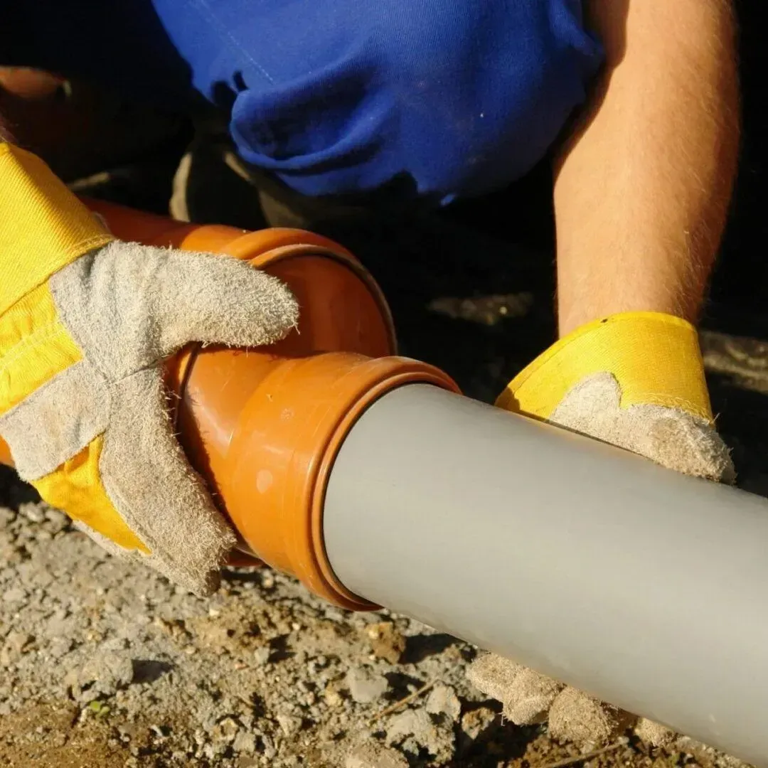 A man wearing yellow gloves is working on a pipe