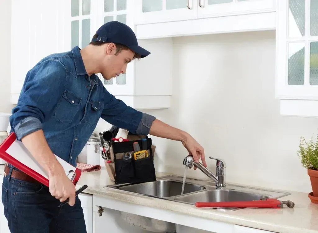 A plumber is fixing a sink in a kitchen.