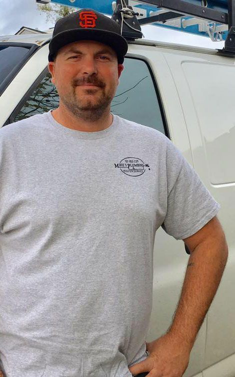 A man wearing a hat and a grey shirt is standing in front of a white van.