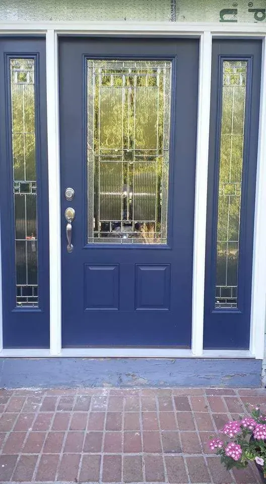 A blue door with stained glass windows is on a brick walkway.