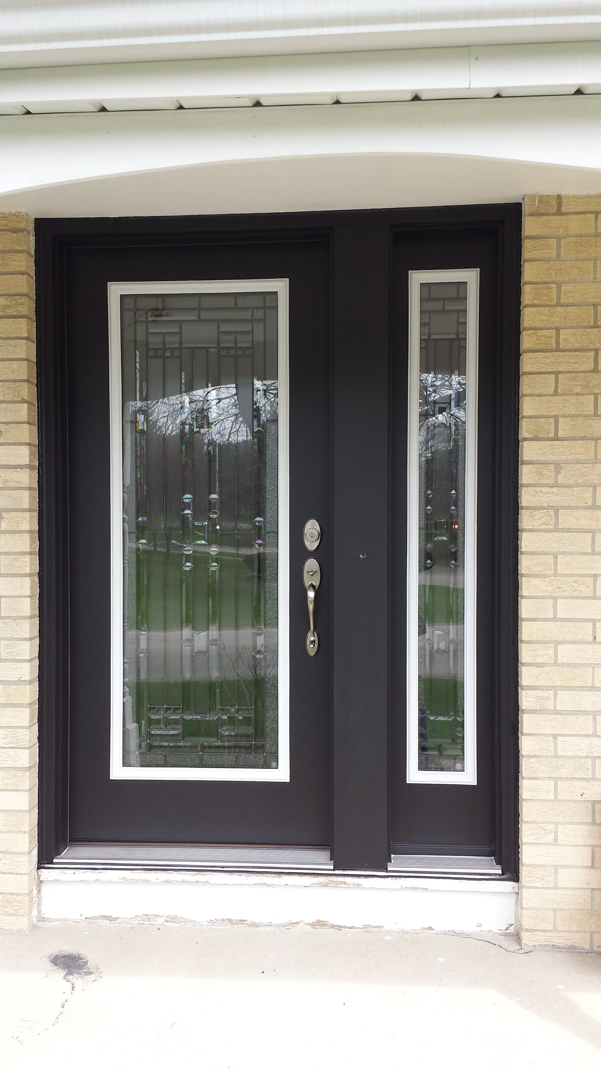 A black door with a stained glass window is on a brick building.