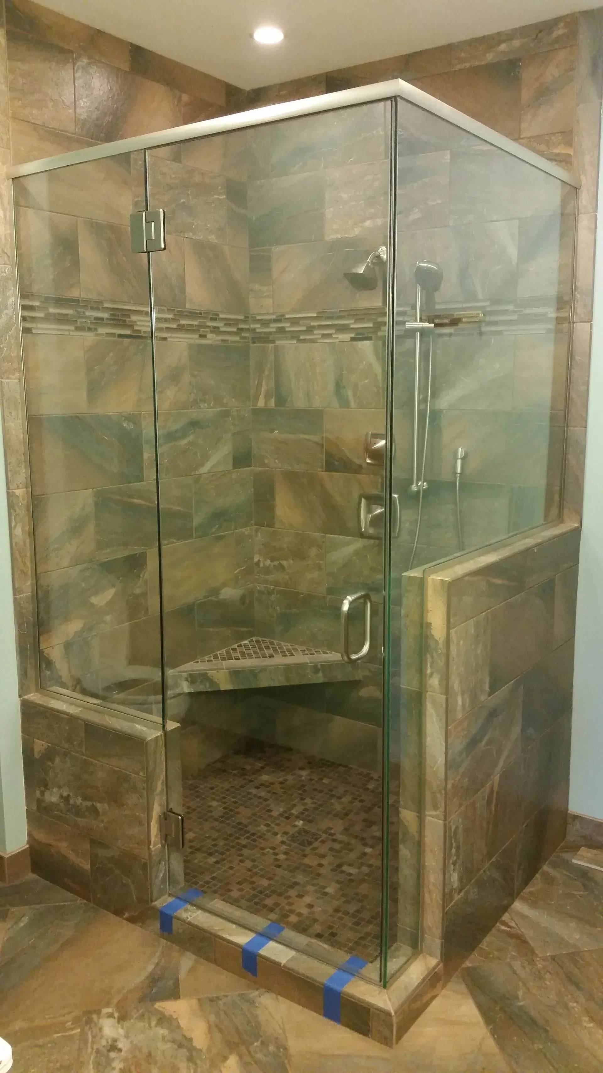 A shower stall with a glass door and a bench in a bathroom.