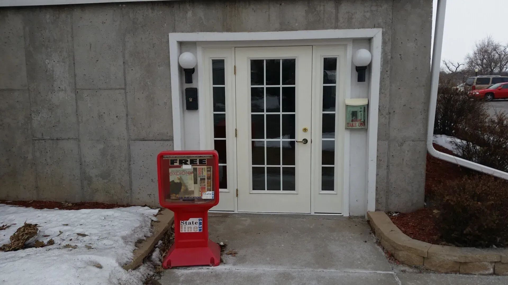 A red vending machine is outside of a building