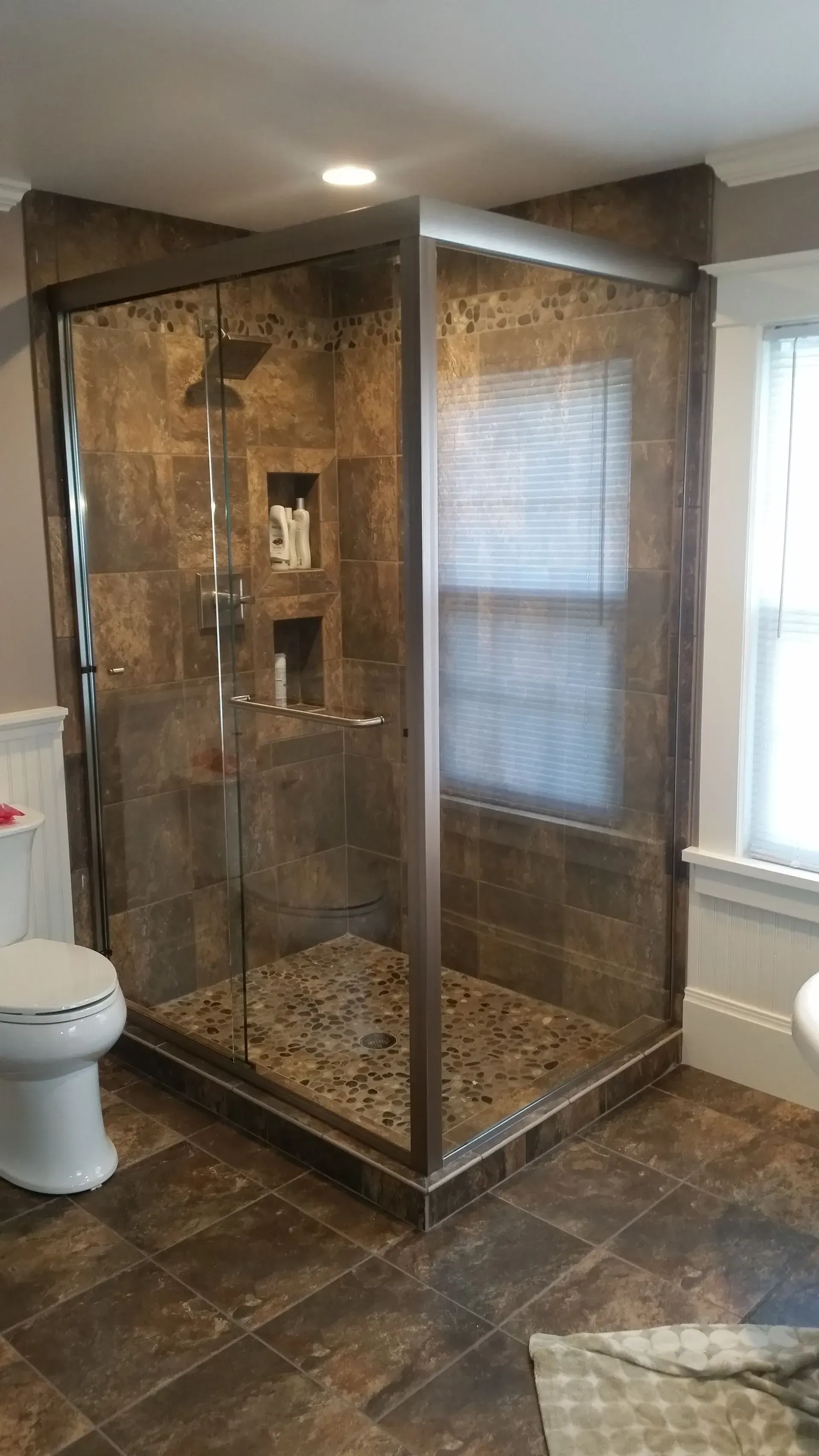 A bathroom with a walk in shower , toilet and window.