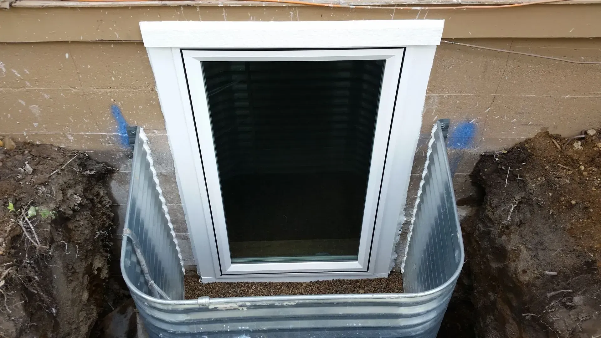 A window is being installed in the basement of a house.