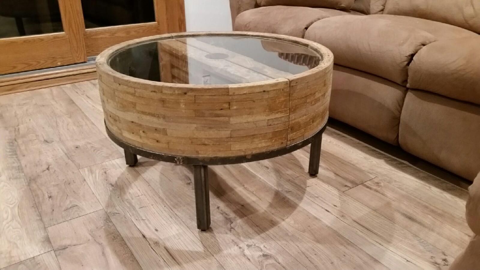 A round coffee table with a glass top is in a living room next to a couch.