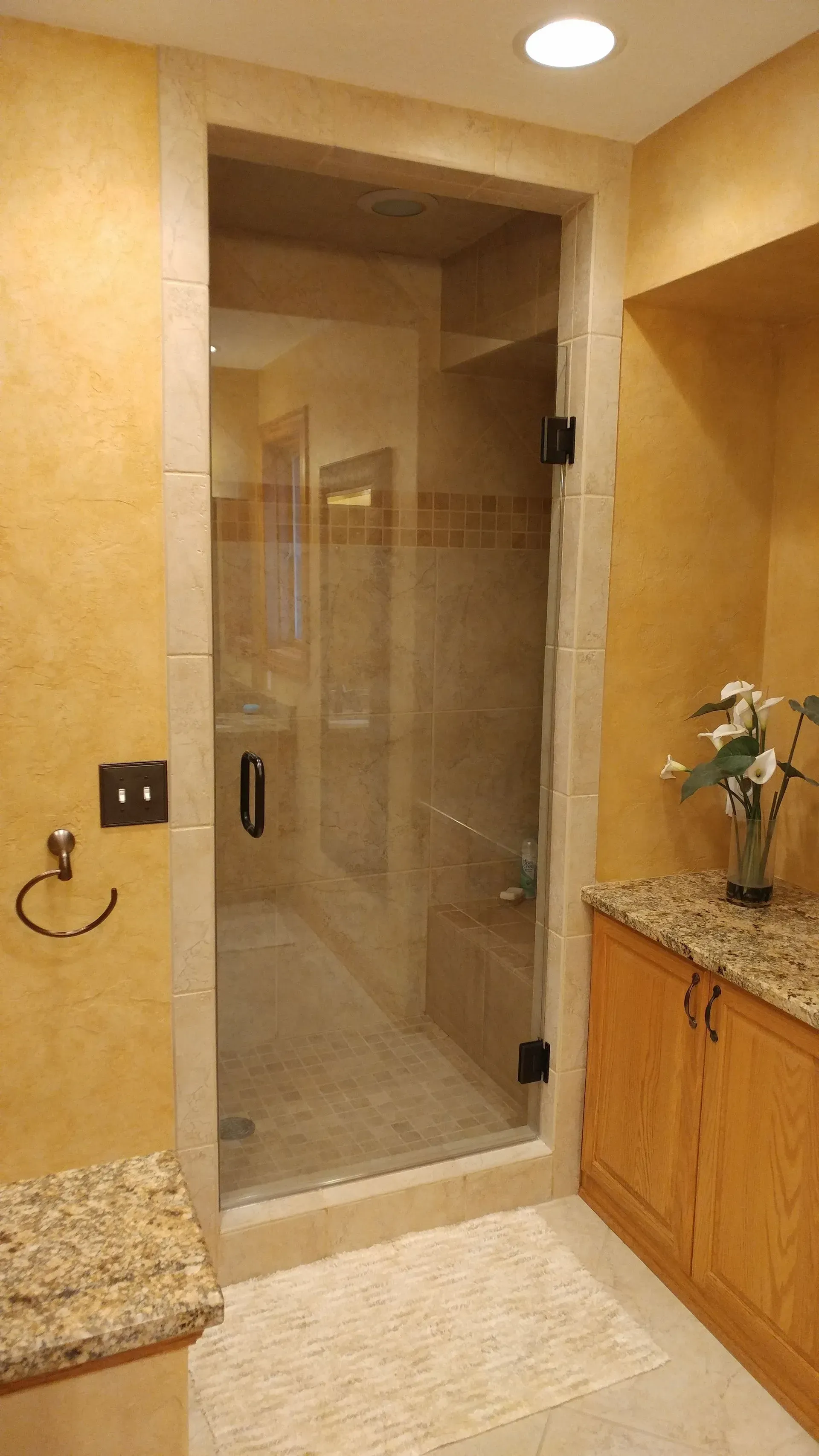 A bathroom with a glass shower door and a granite counter top.