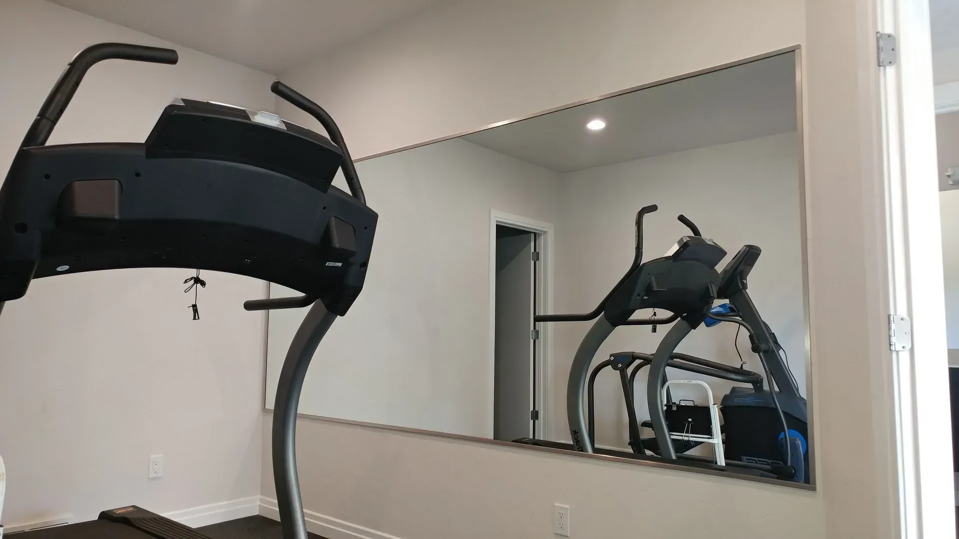 A treadmill is reflected in a large mirror in a gym.