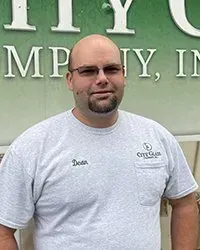 A man wearing glasses and a gray t-shirt is standing in front of a green sign.
