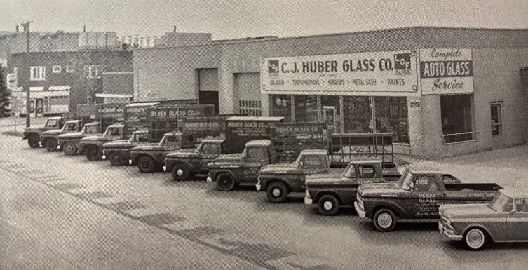 A black and white photo of a row of trucks parked in front of a glass company
