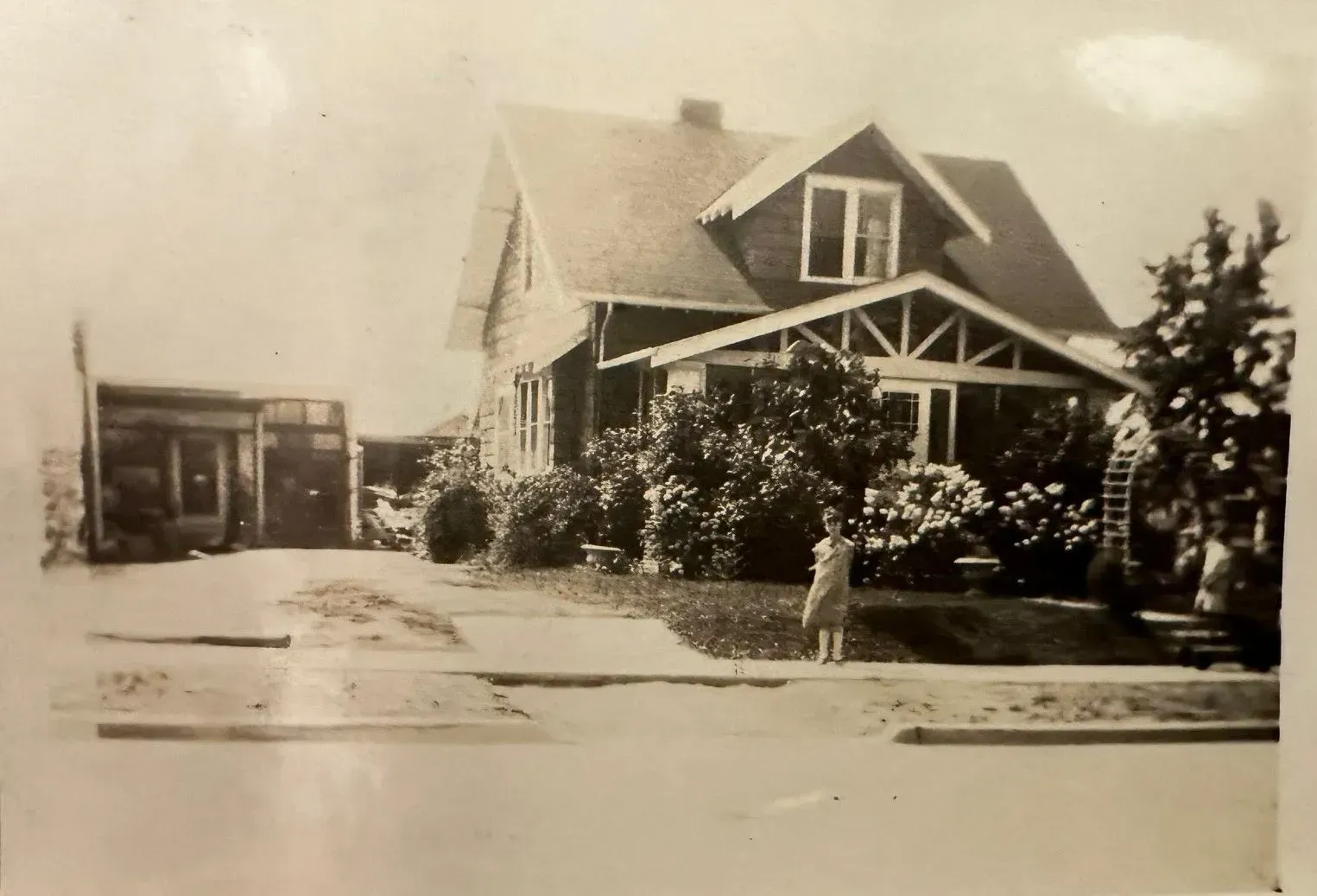 A black and white photo of a house with a girl standing in front of it.