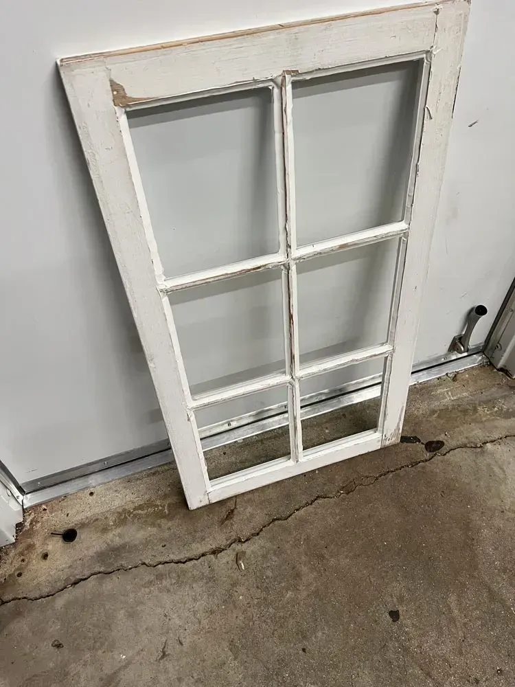 A white window frame is sitting on a concrete floor.
