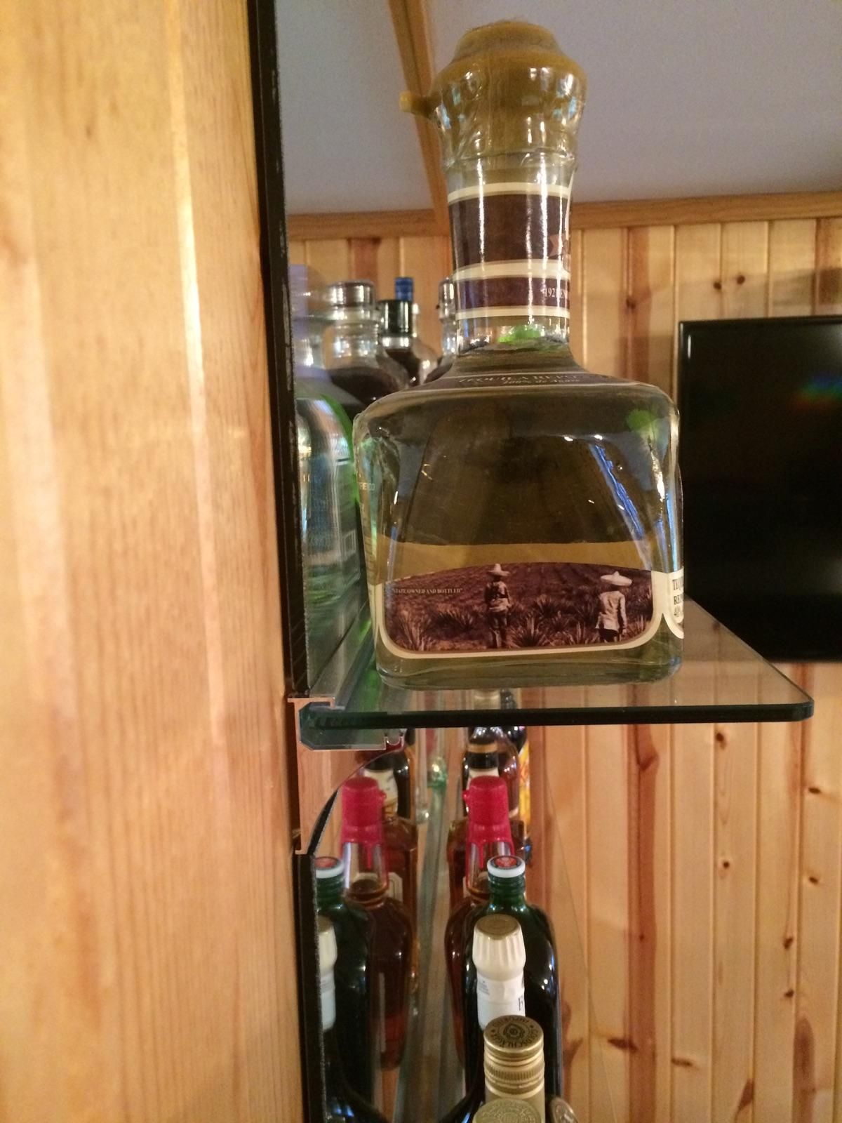A bottle of tequila sits on a glass shelf surrounded by other bottles