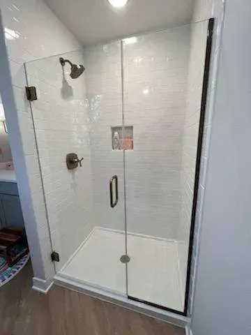 A bathroom with a walk in shower with a glass door and a shower head.