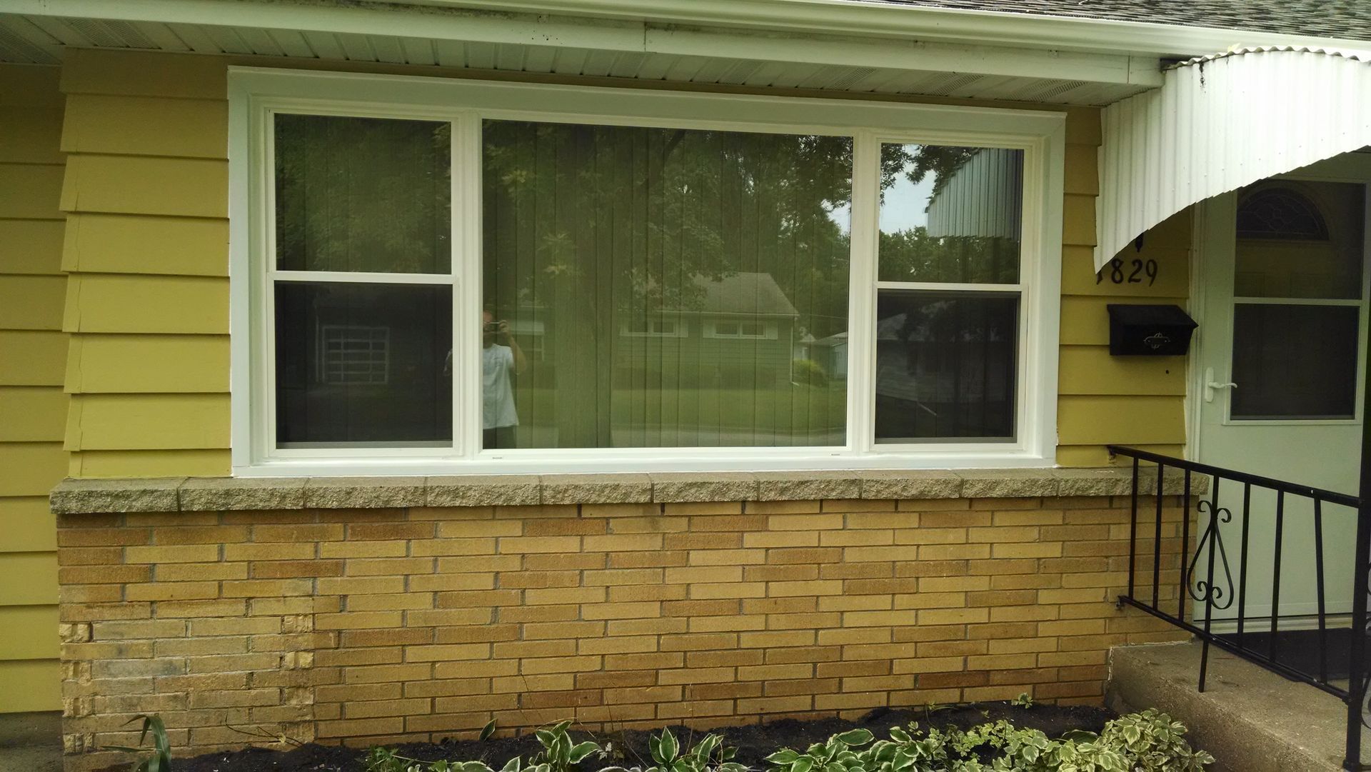 A yellow house with a white window and a white awning.