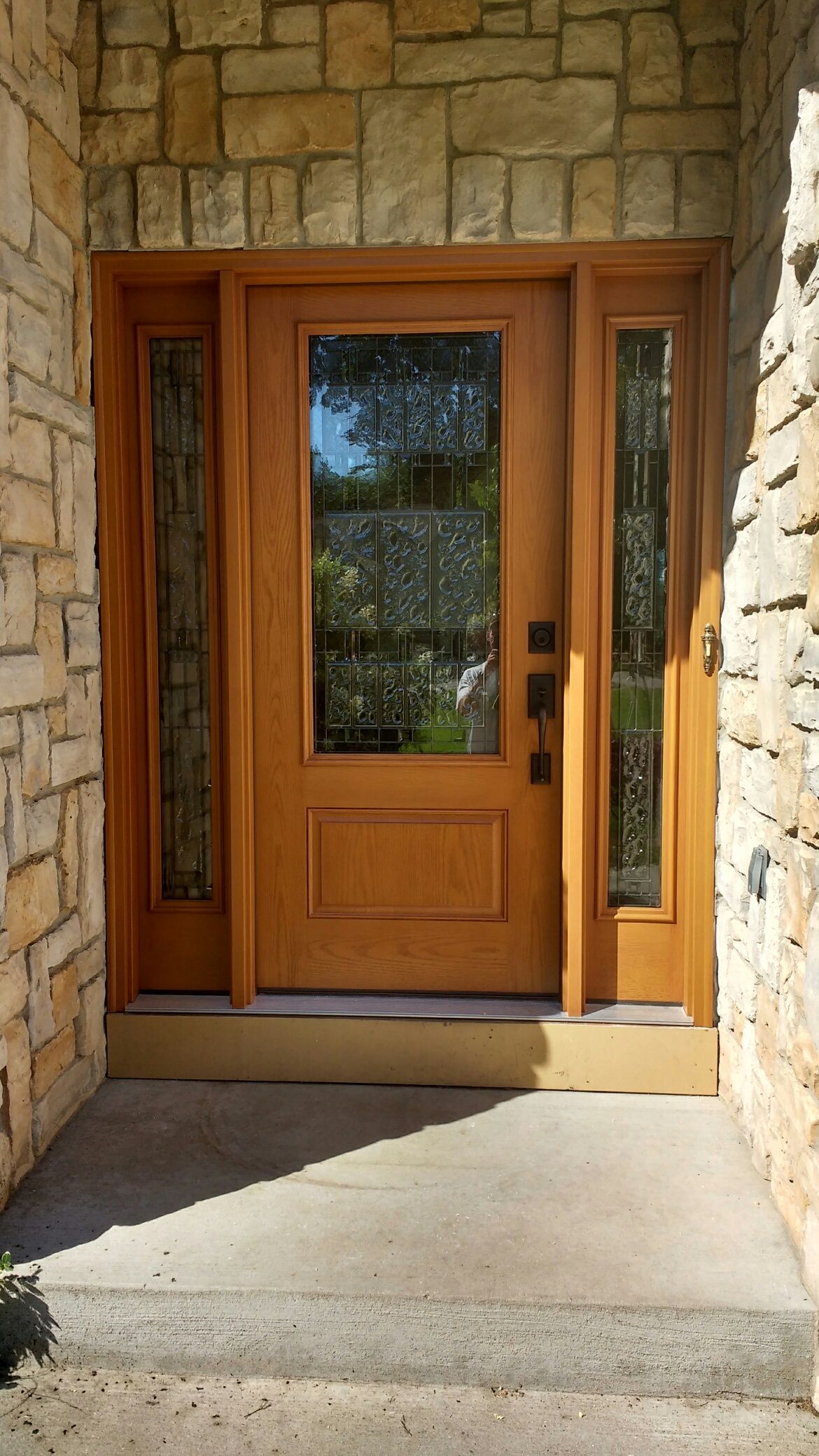 Wooden front door with sidelights, set in stone facade, concrete steps.