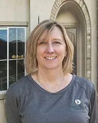 A woman in a gray shirt is smiling in front of a building.