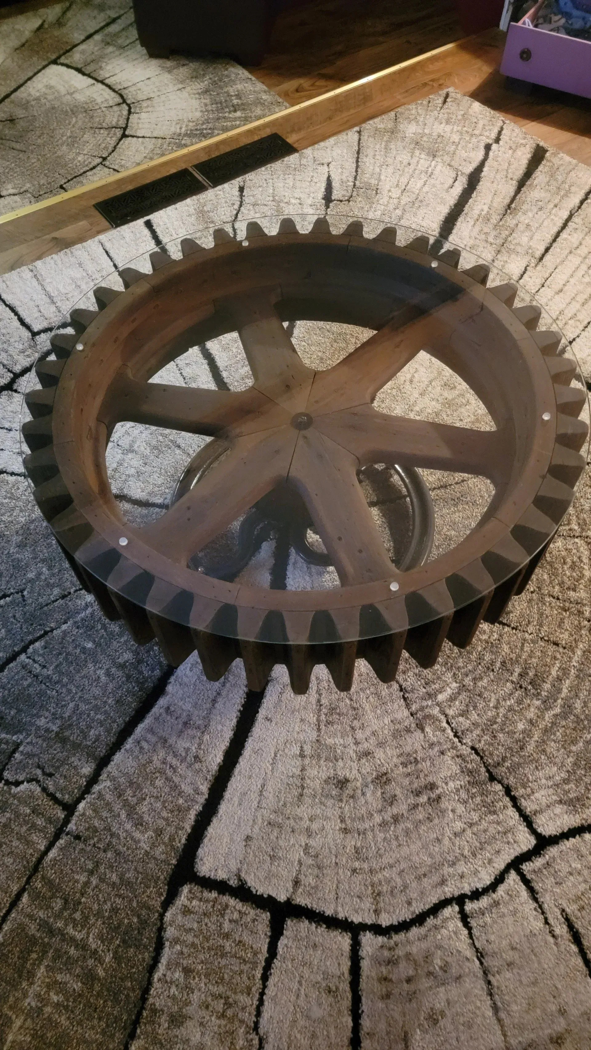 A coffee table made out of a gear on a rug.