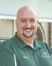 A bald man with a beard is wearing a green polo shirt and smiling.