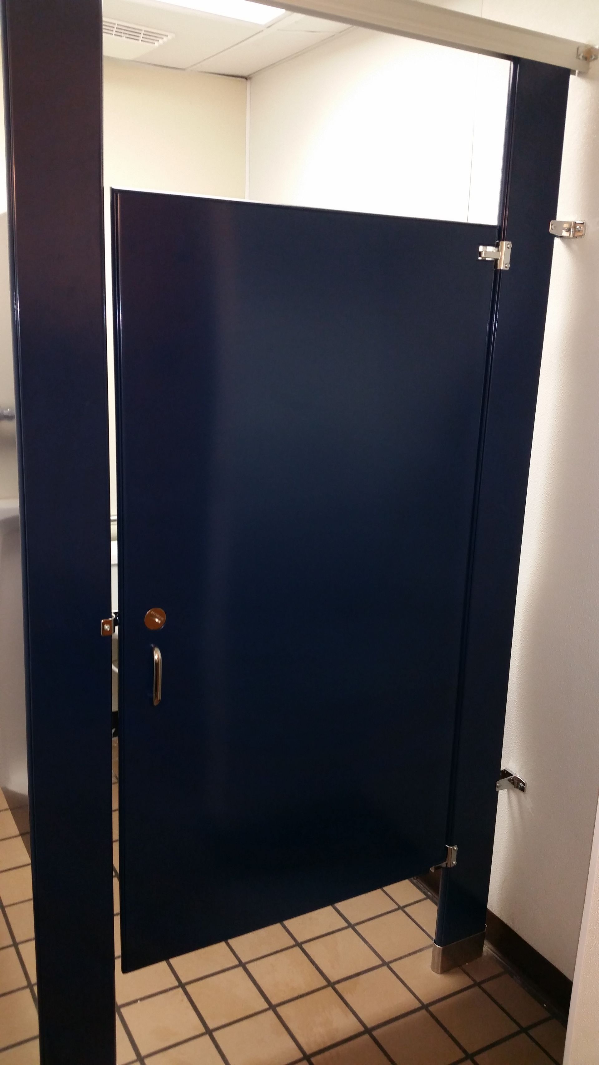 A blue toilet cubicle in a public restroom with a tiled floor.
