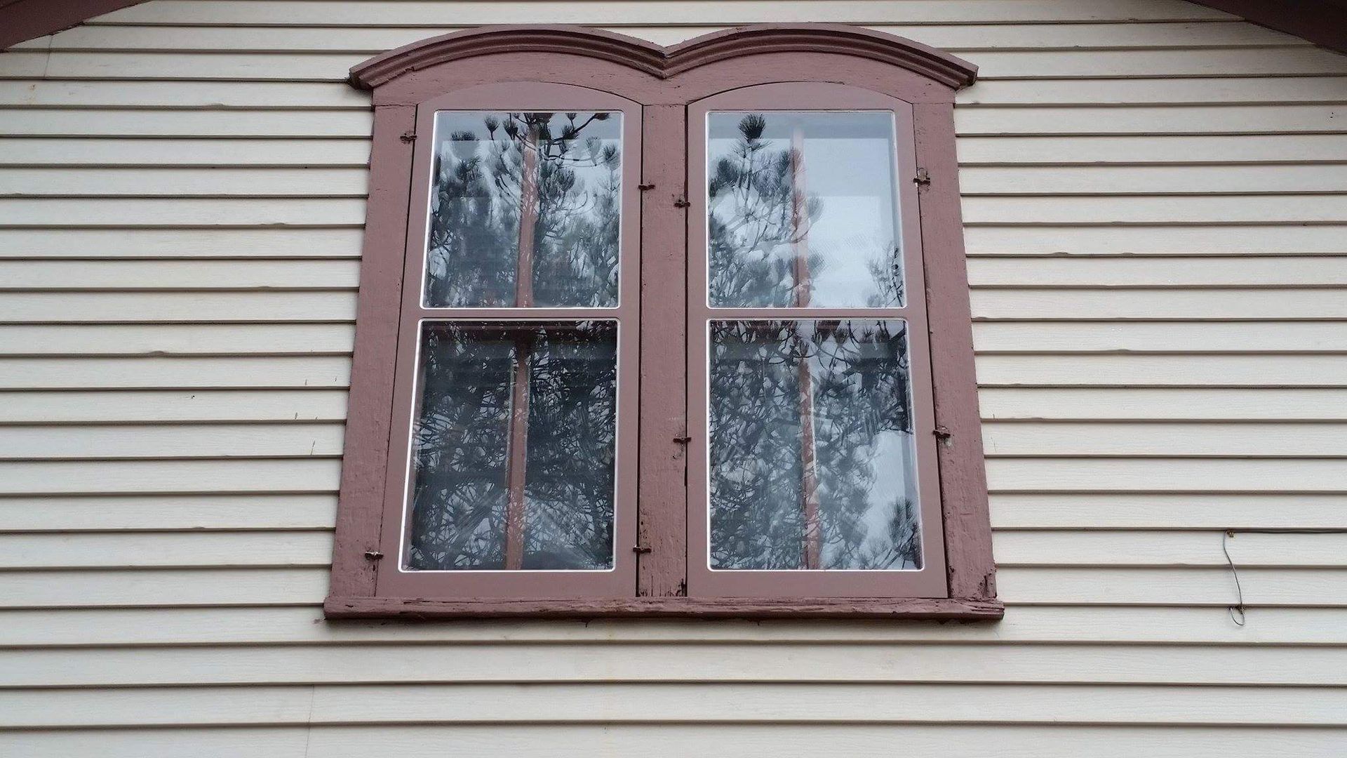 A window on the side of a house with trees reflected in it