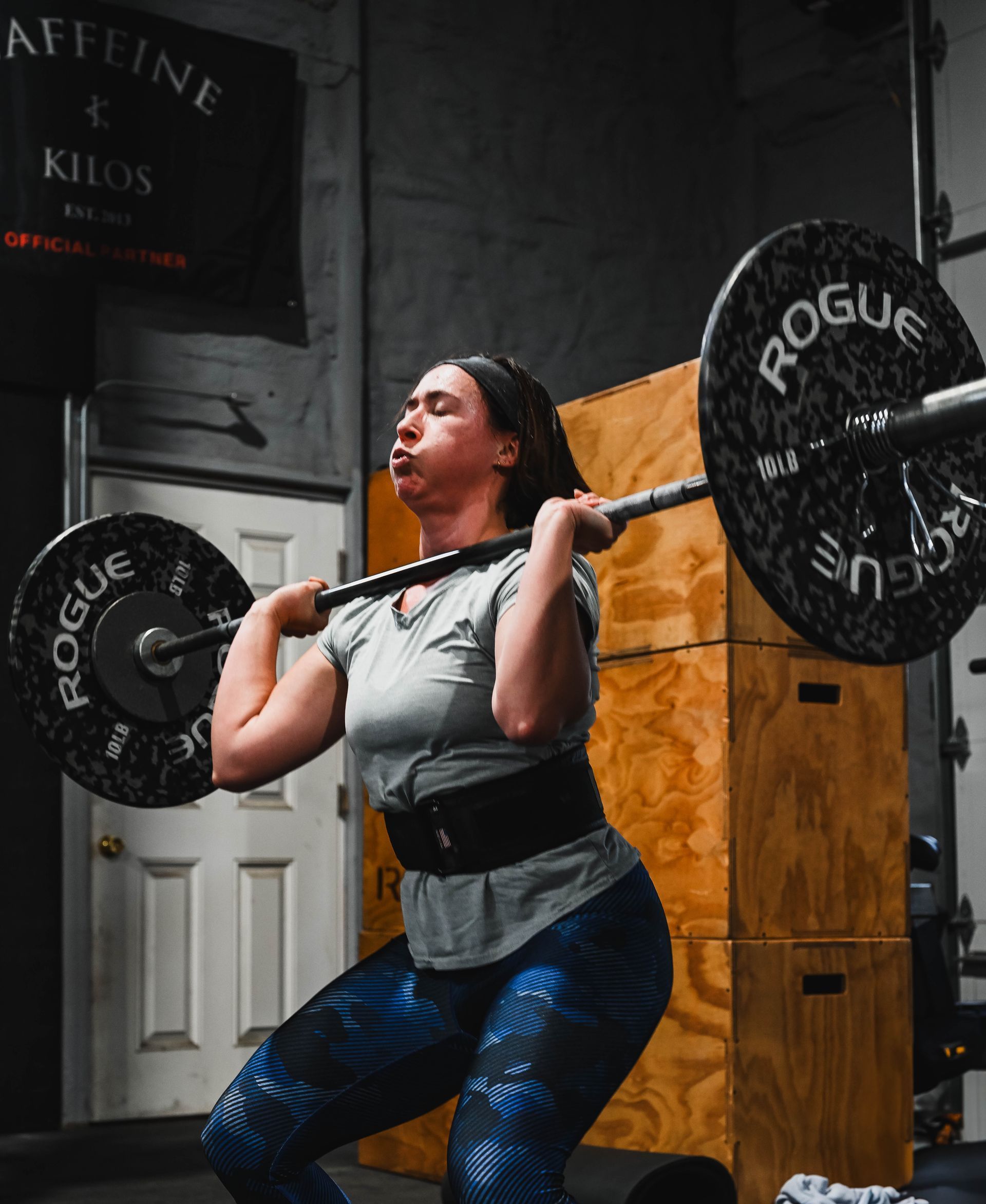 Woman lifting a barbell overhead, wearing a weightlifting belt, in a gym.