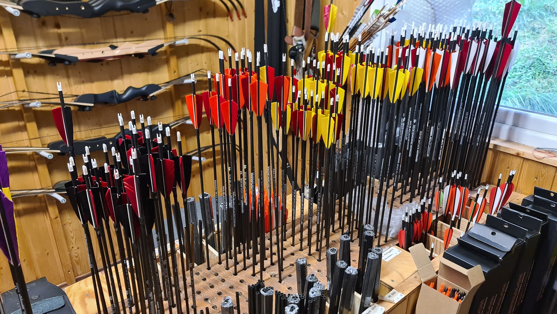 Pfeile mit verschiedenfarbigen Federn, in Haltern angeordnet, in einem Bogenschießgeschäft mit Holzwänden.