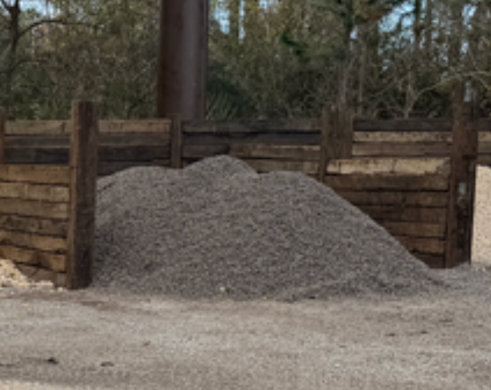A large pile of grey gravel contained within a wooden storage bin in an outdoor setting.