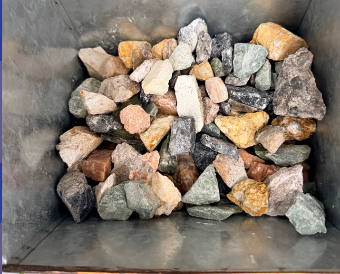 A high-angle view of a metal container filled with an assortment of multi-colored, angular river rocks and stones.