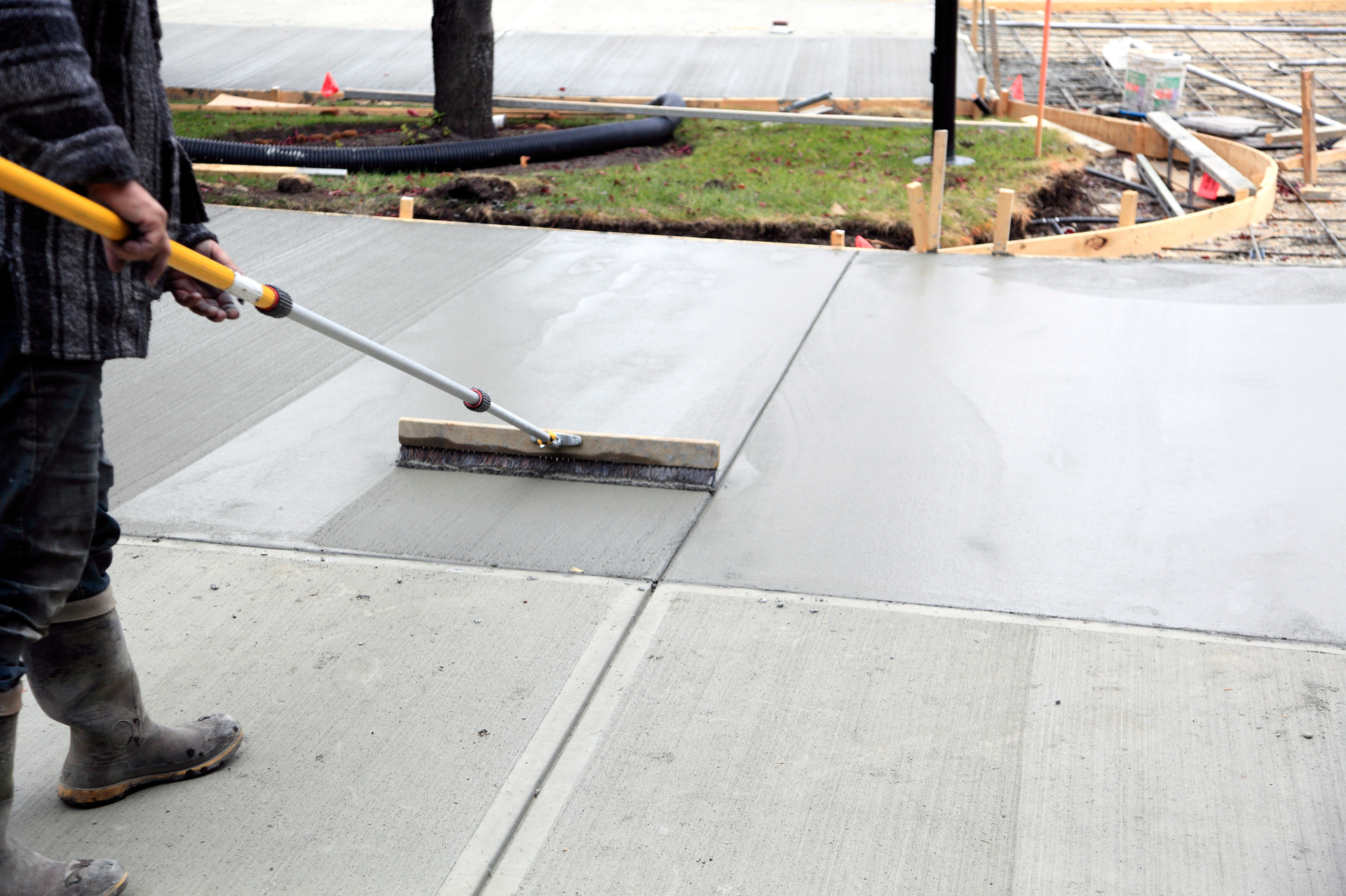 Worker using a long-handled squeegee to smooth wet concrete on a construction site