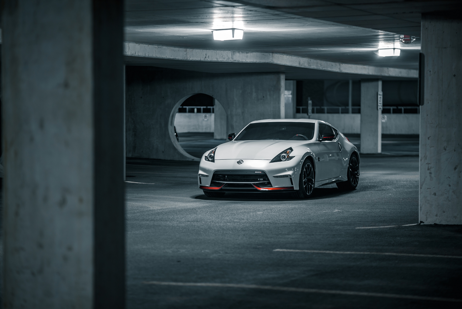 White sports car parked in a dim concrete parking garage under overhead lights