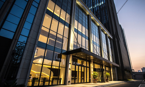 Modern office building exterior with glass windows, lit interior, and dusk sky.