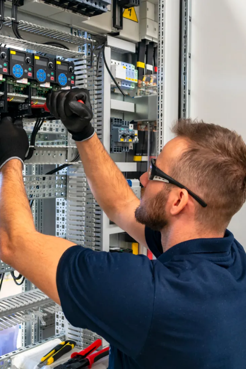 Electrician working on electrical panel, wearing safety glasses and gloves.