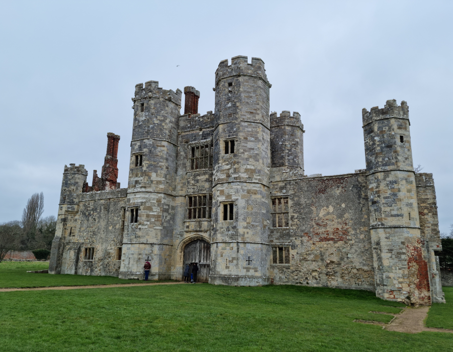 The stone façade and towers of Titchfield Abbey in Hampshire, set against an overcast sky with a grassy foreground.