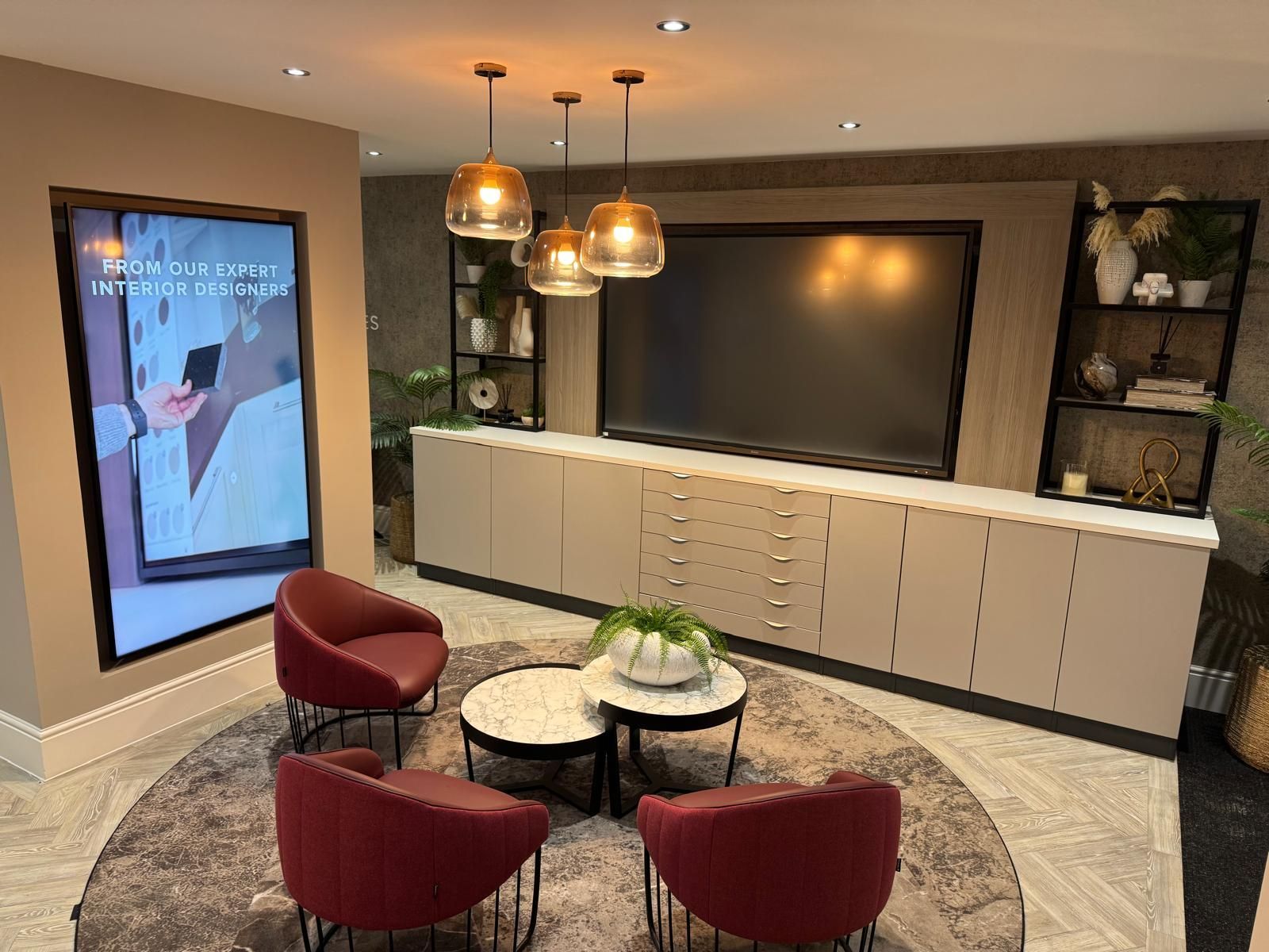 A modern living room with a large screen, tan cabinets, three chairs, and two small round tables on a patterned rug.