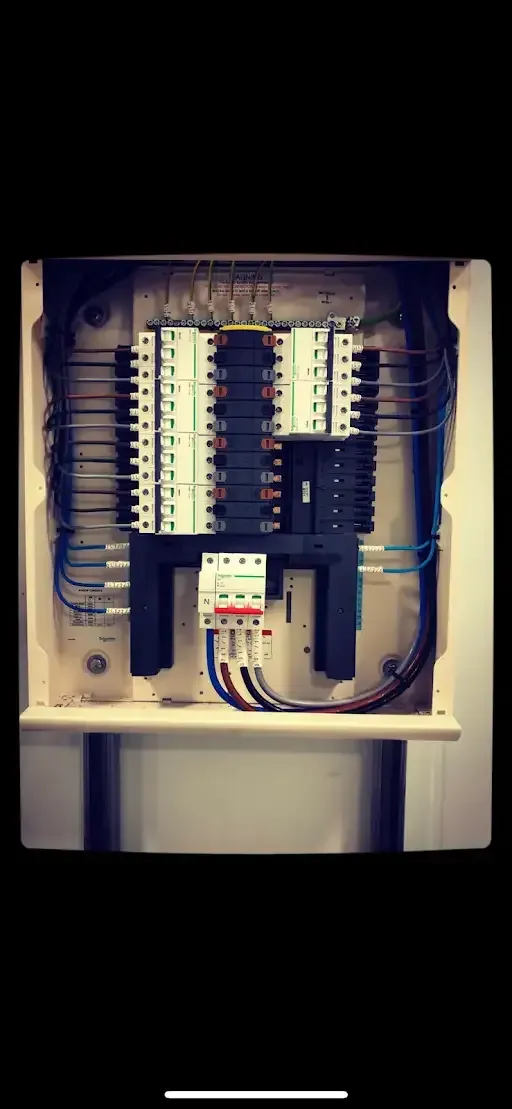 Electrical panel with circuit breakers and wiring inside a white enclosure.