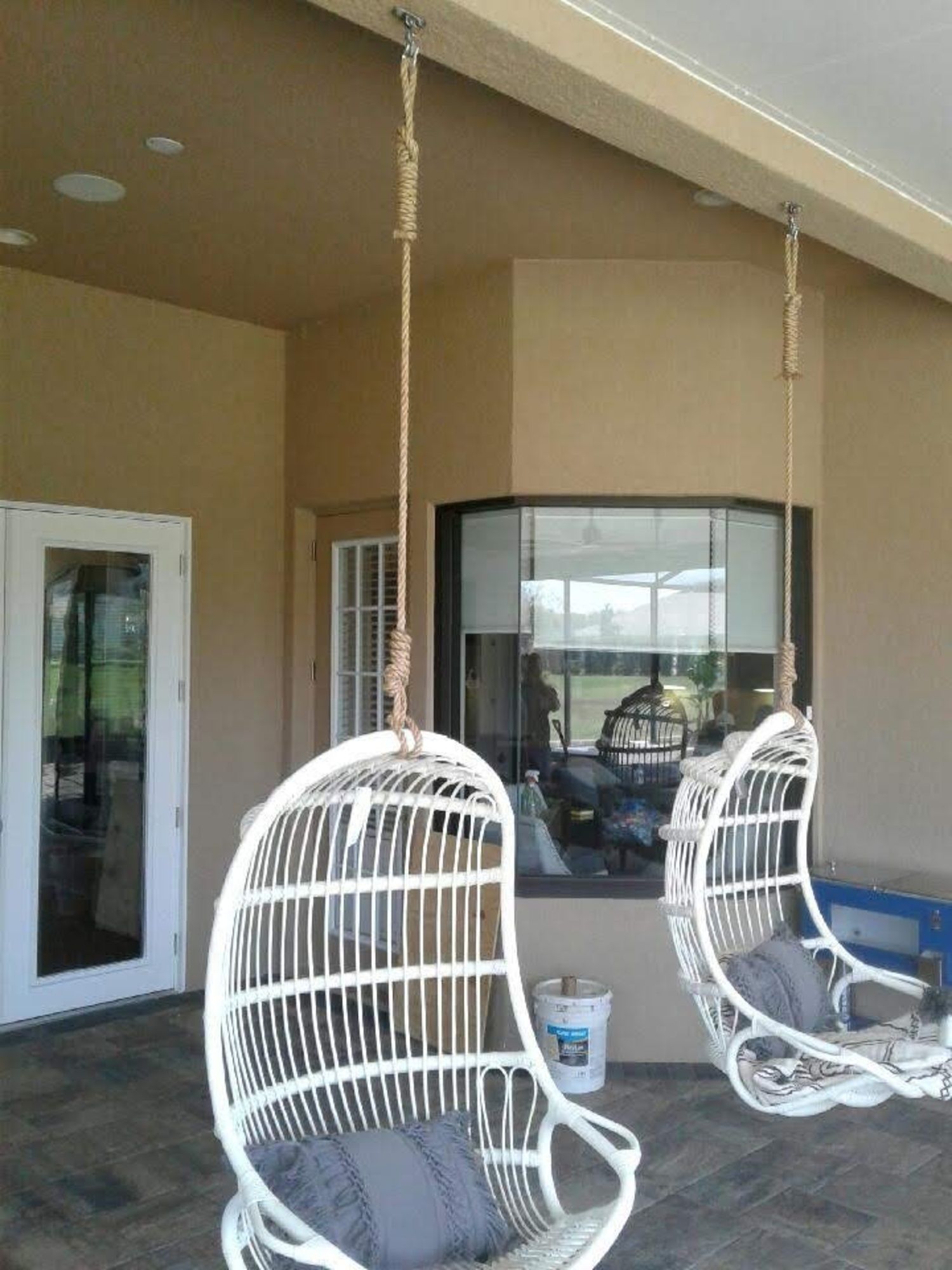 two white wicker chairs are hanging from the ceiling on a patio .
