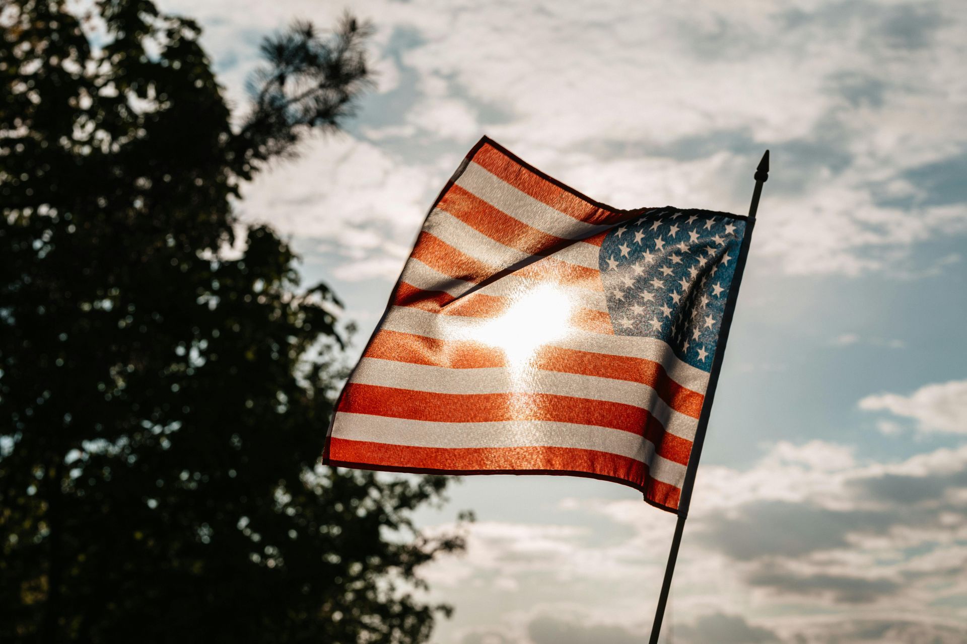 American flag waving in sunlight against a cloudy sky.