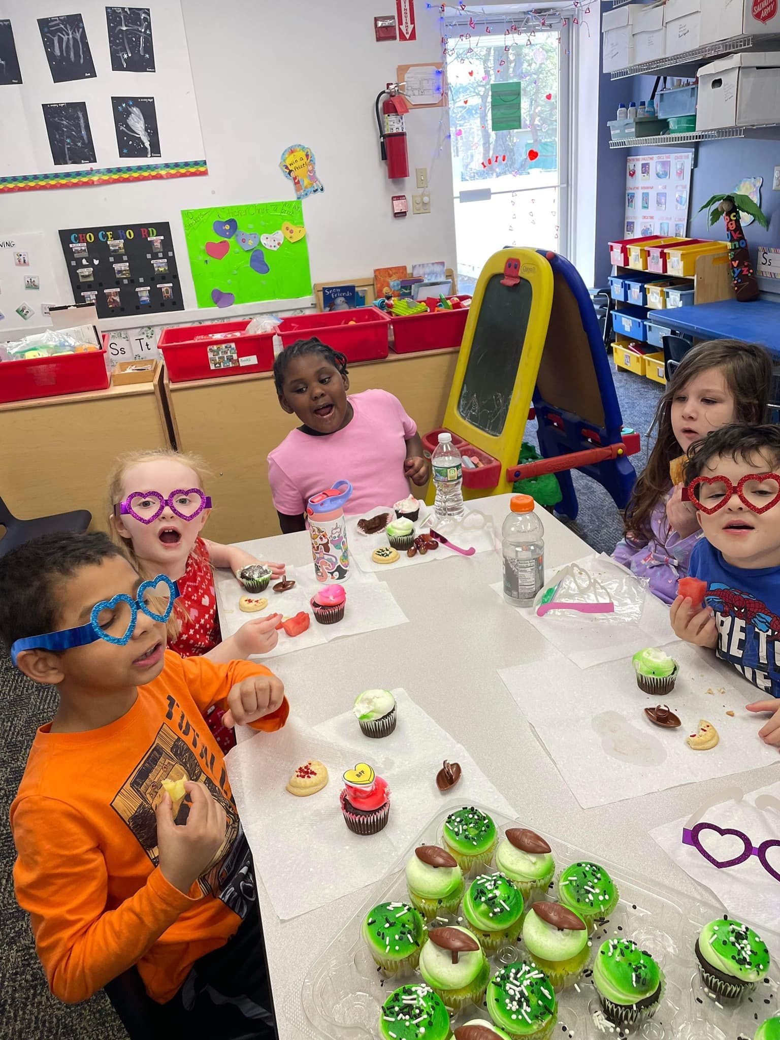 A group of children are sitting at a table decorating cupcakes.