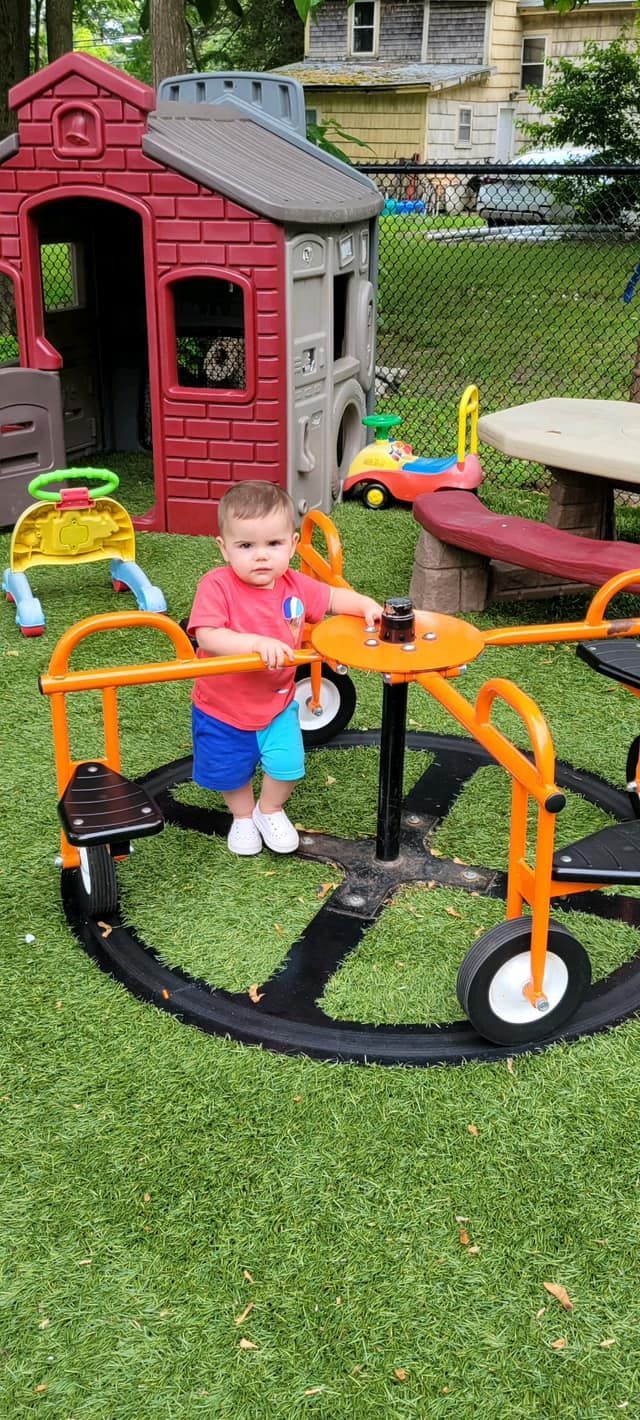A little boy is sitting on a merry go round in a playground.