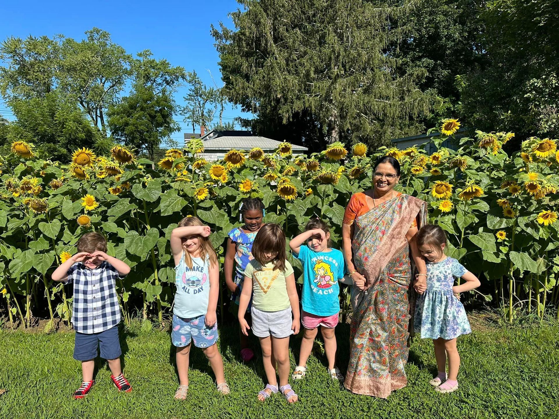 A group of children are standing in front of a field of sunflowers.
