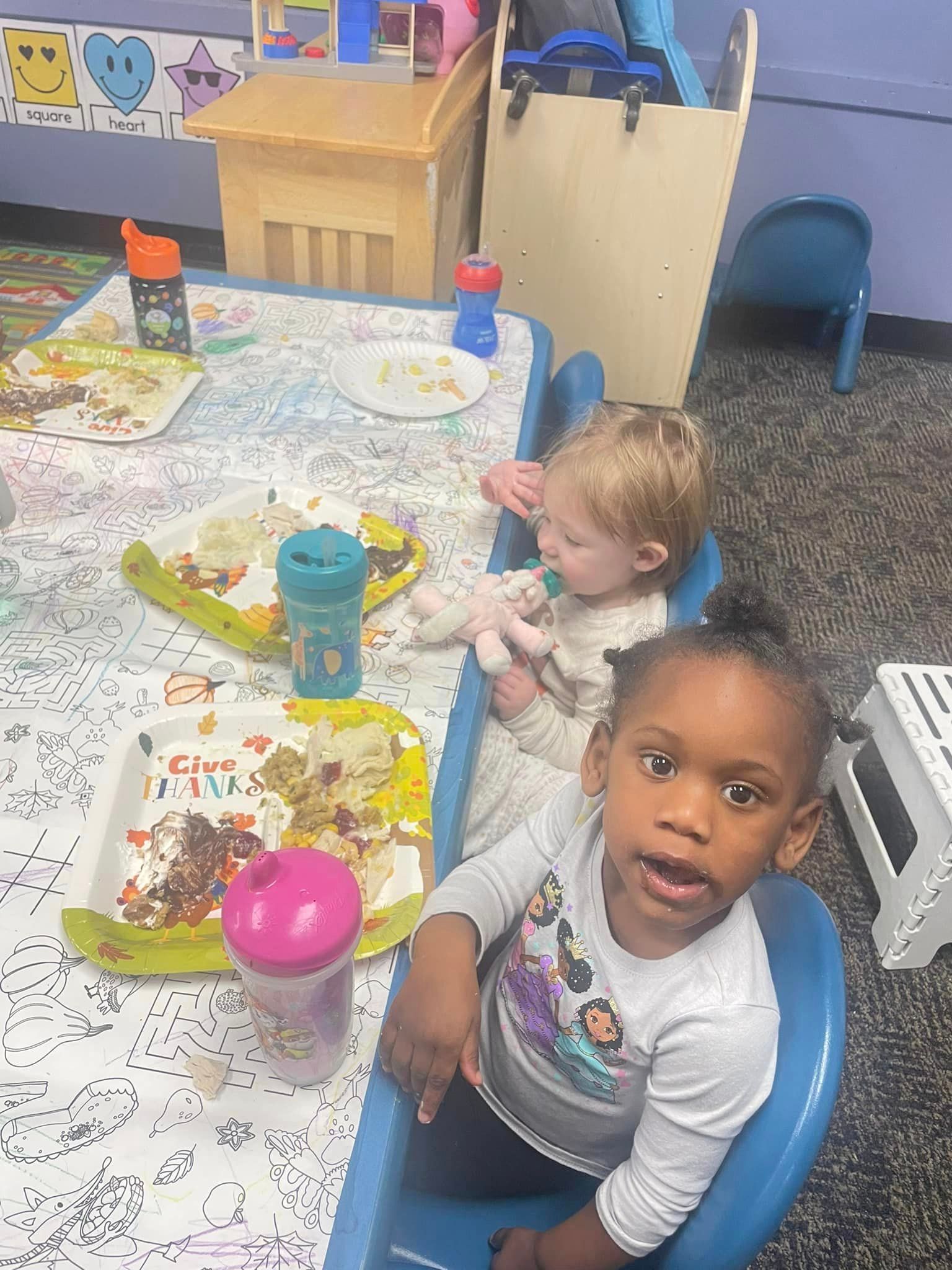 Two little girls are sitting at a table with plates of food.