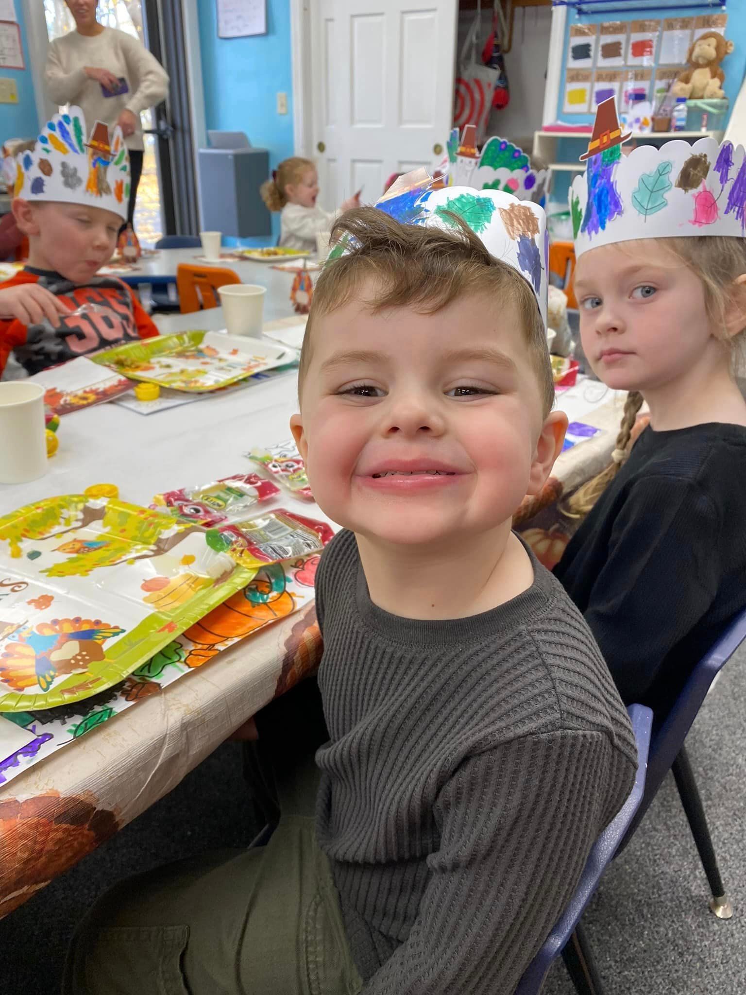 A group of children are sitting at a table wearing party hats.